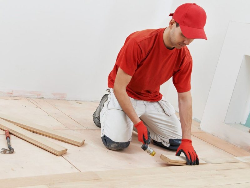 A man dressed in red is working on a wooden floor, representing a flooring service in Honolulu, HI.