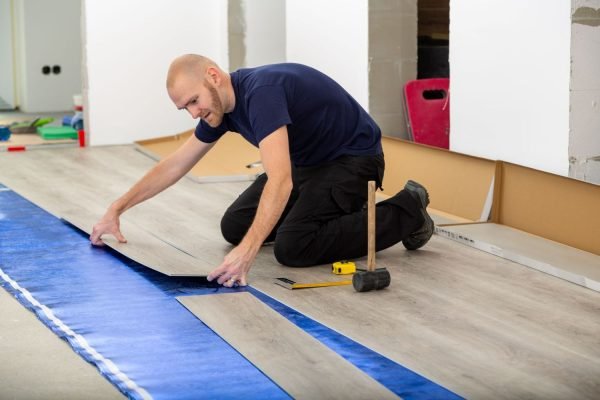 A man is positioning a blue tarp on the floor for luxury vinyl tile installation in Honolulu, HI.