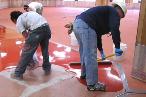 Two men using a paint roller to apply red paint to a floor, part of an epoxy tile flooring service in Honolulu, HI.